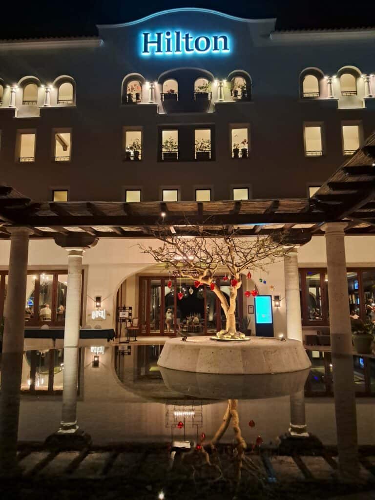 View of fountain in open air lobby and Hilton sign lite up at night.