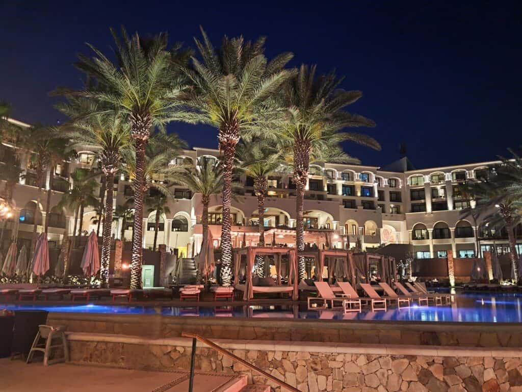 The Hilton Los Cabos lit up at night with palm trees, and loungers around the pool.