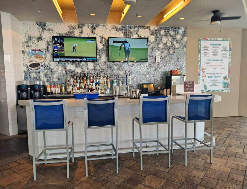 Pool bar with 2 TV screens on the back wall and 4 bar stool chairs.