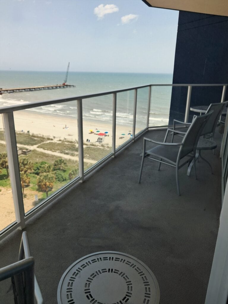Balcony with chairs and table with view of the ocean and a pier under construction.