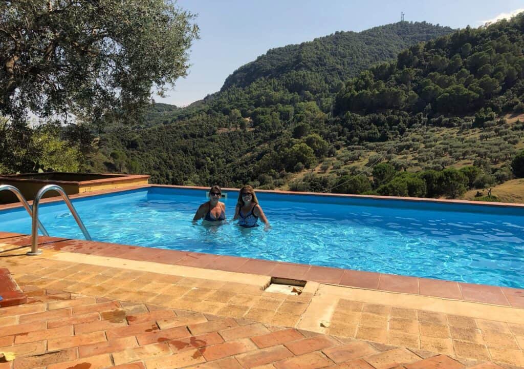 Two women in the swimming pool with hills and trees behind them at Le Puzzle near Santa Severina.