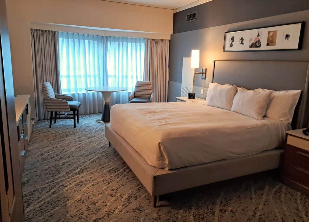 The Residences by Hilton Club review of a studio room with a king size bed, a table and two chairs, and nightstands by the bed.