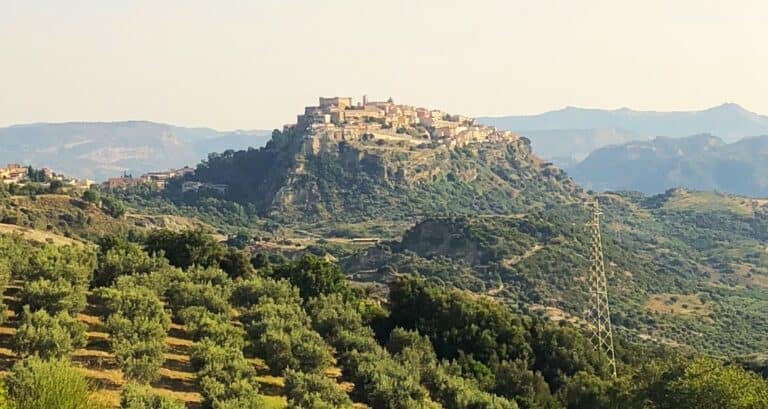 Medieval town of Santa Severina sitting on top of hill surrounded by mountains and vineyards.