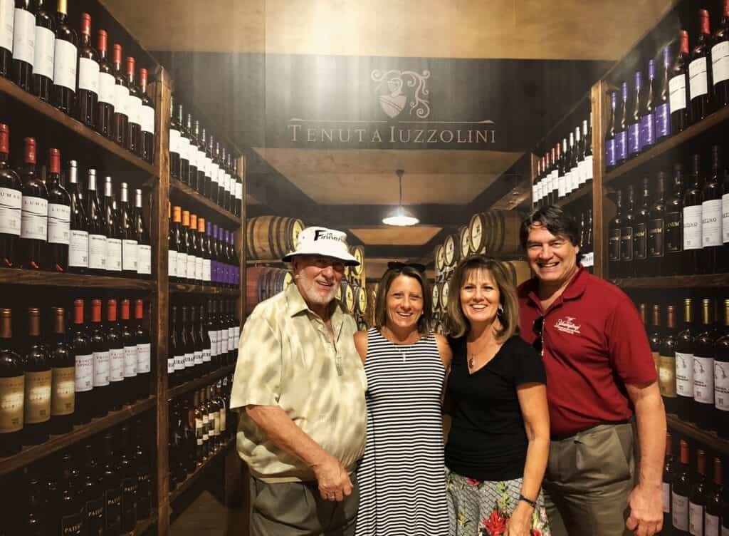 Four people standing in a wine cellar surrounded by bottles of wine and wine barrels in the background at Tentuat Iuzzolini near Santa Severina.