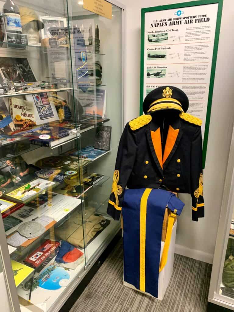 A military dress uniform with hat and artifacts on display at the military museum.