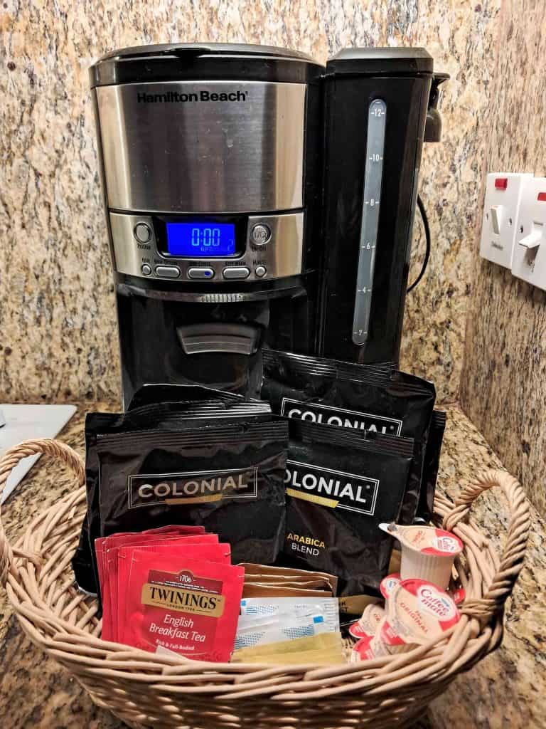 Hamilton Beach coffee maker and basket filled with coffee packets, tea bags, sugar, and creamer,