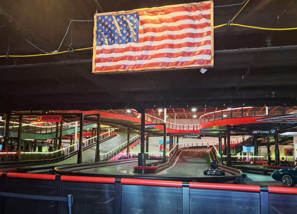Large American flag hanging above the multi-level electric go kart racing track.